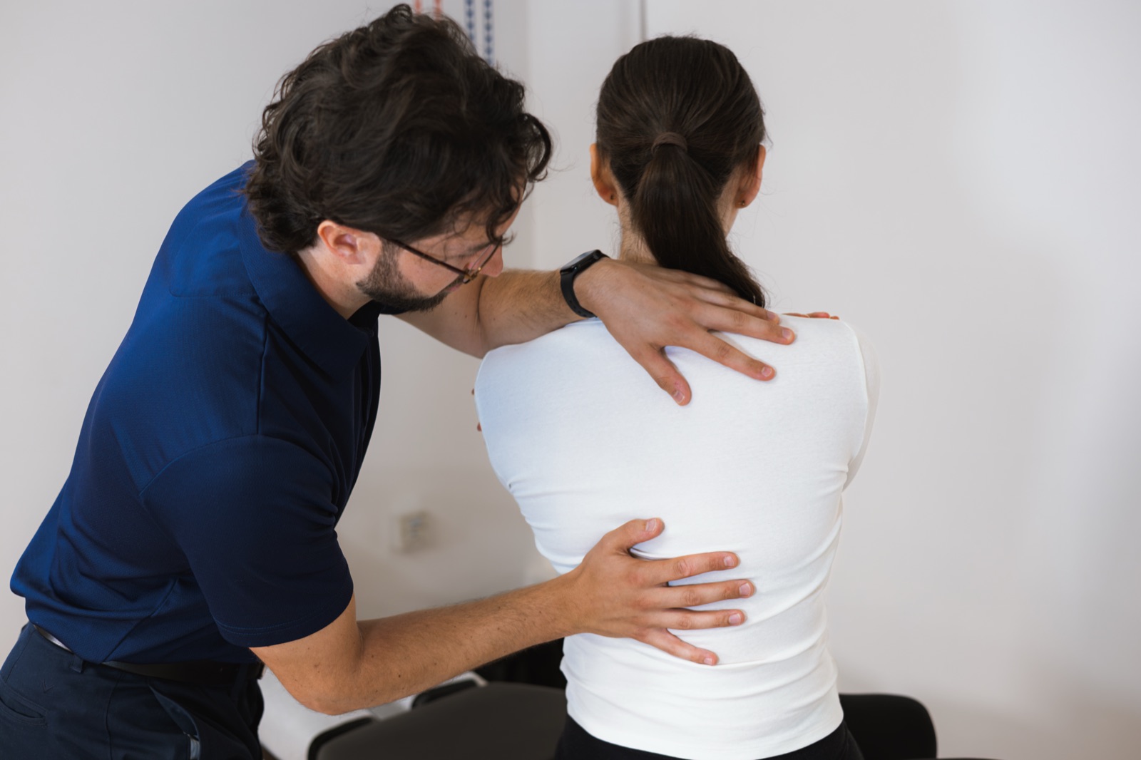 Tom assessing a patient's spine as they bend forwards, one hand at the lower back